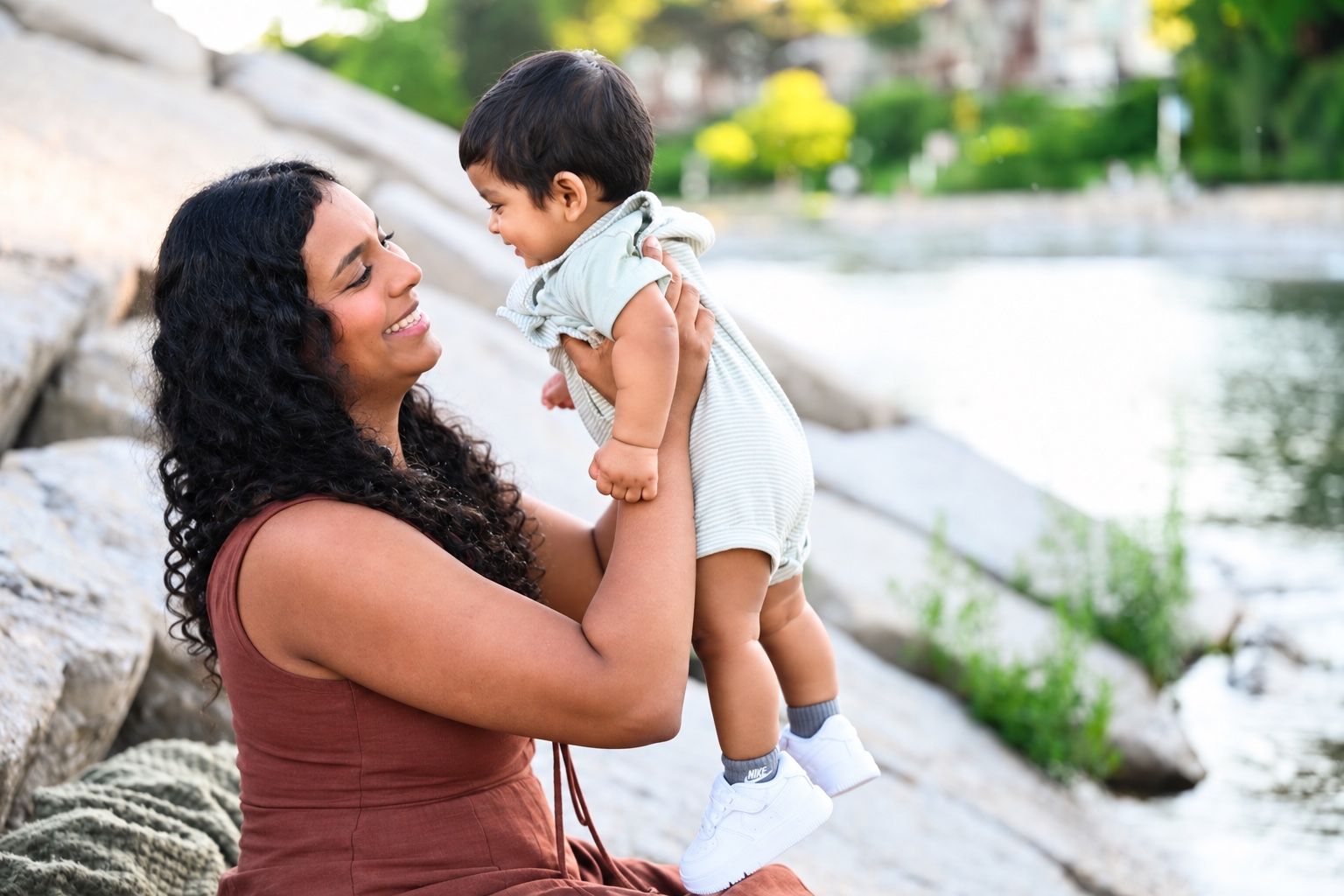 Cynthia smiling as she lifts her baby by the water